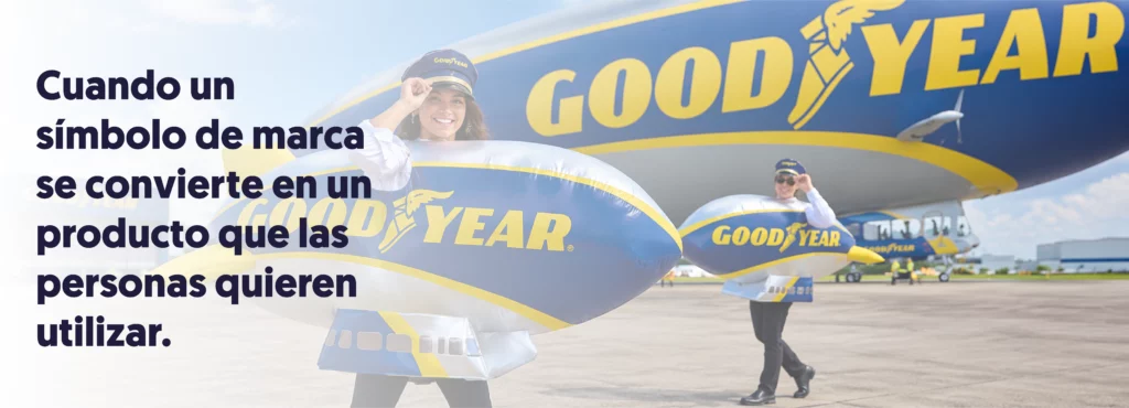 Dos personas con disfraces hinchables del dirigible Goodyear posan delante del dirigible de la marca